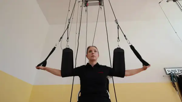 Kobieta ćwiczy z użyciem systemu podwieszeń, wykonując ćwiczenie angażujące mięśnie w sposób przypominający skurcz izotoniczny.