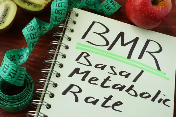 Notatnik z napisem BMR (Basal Metabolic Rate), obok jabłko, kiwi i miarka krawiecka. Obliczenia BMR, jak wzór Harrisa Benedicta, pomagają zrozumieć metabolizm.