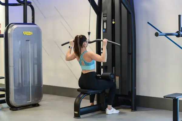 Kobieta wykonuje ćwiczenie ściąganie drążka wyciągu górnego, budując siłę pleców.