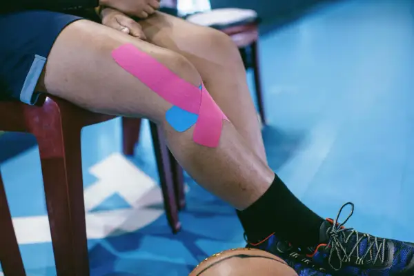 Osoba z chondromalacją rzepki stosuje kinesiotaping. Różowe i niebieskie plastry na kolanie wspierają ćwiczenia.