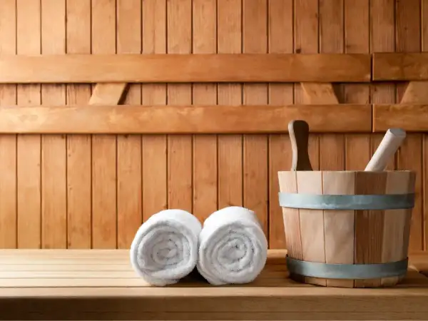Drewniana sauna z dwoma ręcznikami i wiadrem. Odpoczynek w saunie to relaks i oczyszczenie.