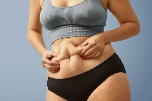 Kobieta z "skinny fat" sylwetką, chwytająca fałd skóry na brzuchu.