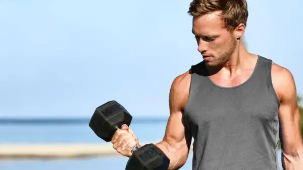 Mężczyzna ćwiczy biceps z hantlem, zastanawiając się, ile serii na biceps w tygodniu da najlepsze efekty.