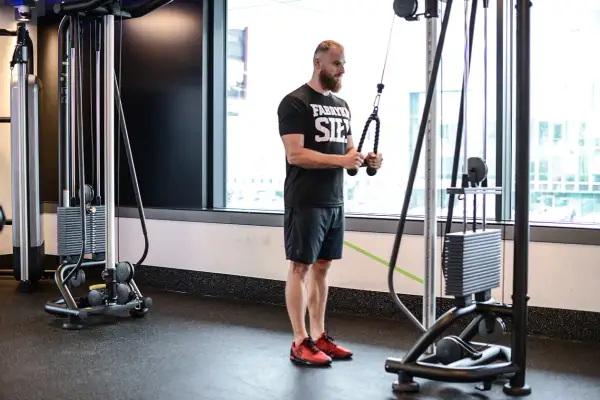 Mężczyzna wykonuje ćwiczenie triceps extension na maszynie typu cable cross.
