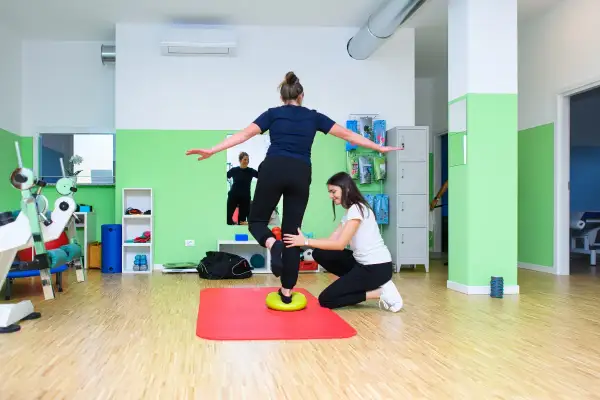 Fizjoterapeutka pomaga pacjentce ćwiczyć równowagę, rozwijając propriocepcję na poduszce balansującej.