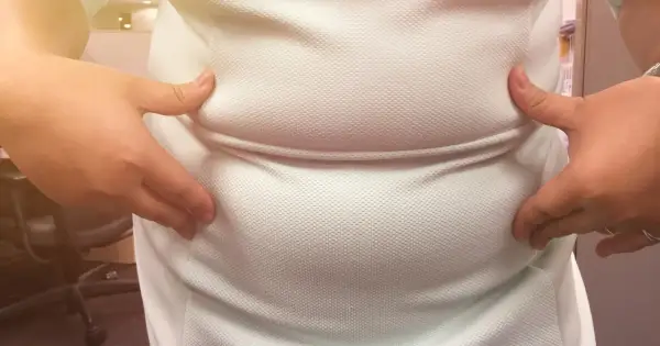 Dłonie ściskają białą koszulkę, uwydatniając zaokrąglony brzuch, który może być oznaką brzucha hormonalnego.
