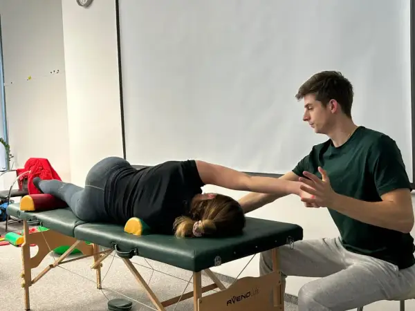 Fizjoterapeuta pomaga pacjentce w ćwiczeniach na stole rehabilitacyjnym, wspierając jej ruchy.