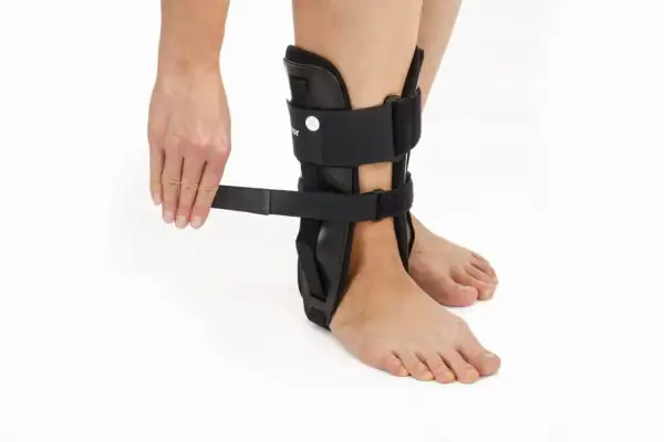 Dłoń zapina czarną ortezę stawu skokowego na nodze.