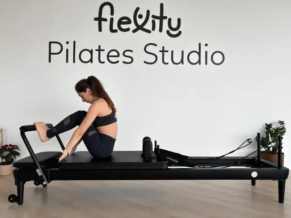 Kobieta ćwiczy na reformerze. Widoczne napisy "Flexity Pilates Studio". To dowód na pilates efekty po miesiącu.