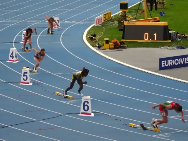 Biegaczki na 400 m walczą o rekord świata. Na bieżni widać zawodniczki w akcji, numery torów i zegar z wynikiem 0.1.