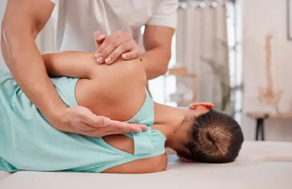 Fizjoterapeuta pomaga pacjentce zmagającej się z neurologiczne bóle mięśni, wykonując delikatny masaż barku.